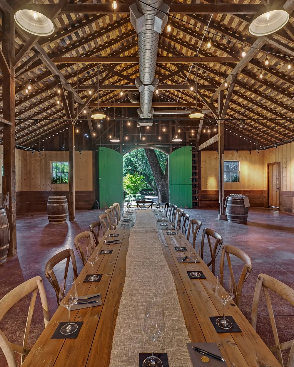 A long table set for a working session in a timber barn, wine barrels along the walls.